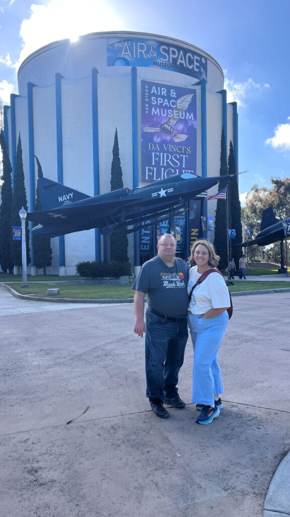 Coup;e stanidng in front of Air and Spce Museum at Balboa Park, in San Diego